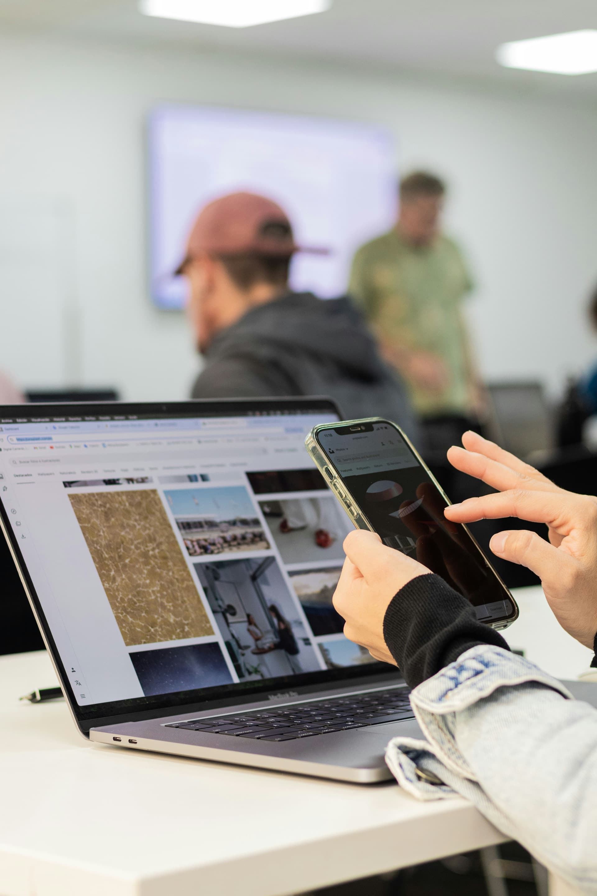 A student using a phone beside a laptop in a classroom
